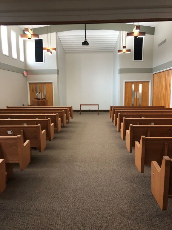 Empty church sanctuary with rows of wooden pews, a simple altar, and overhead crosses.
