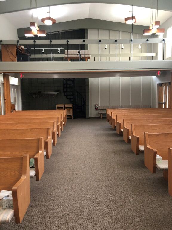 Interior of a church sanctuary with wooden pews, a carpeted aisle, and a balcony in the back.