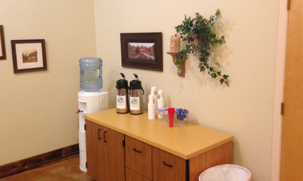 Office break room with water cooler, coffee station, cabinet, and wall decor.