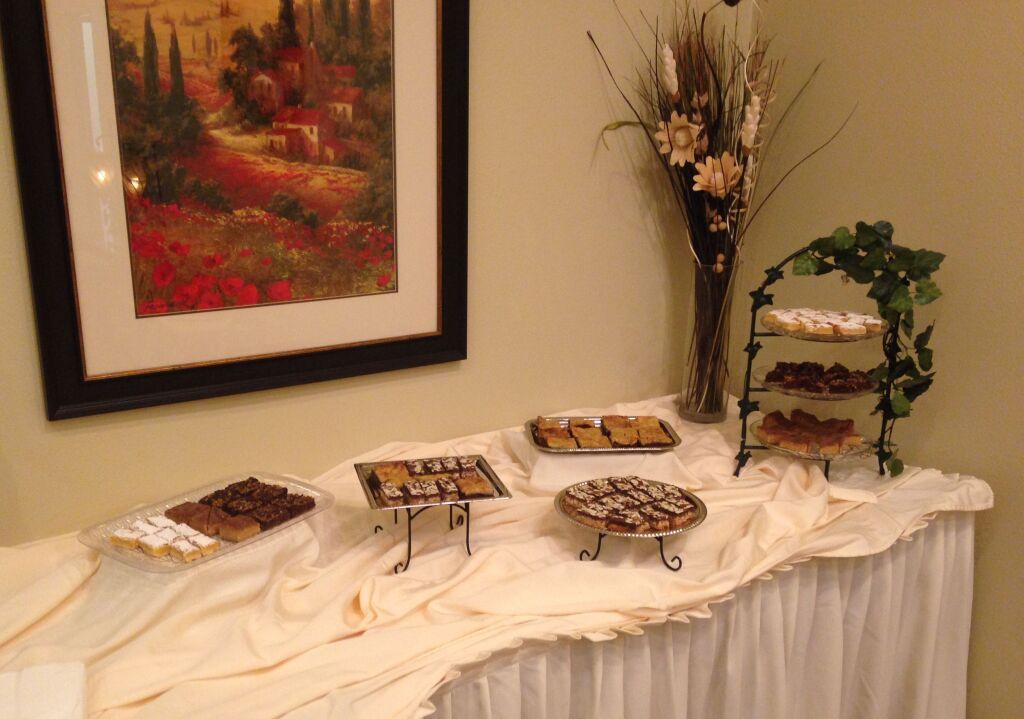 Dessert buffet with various treats on display, framed art, and floral arrangement.