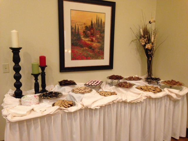 Cookie buffet on a white draped table. Black and red candles, painting, and vase of flowers on the wall.