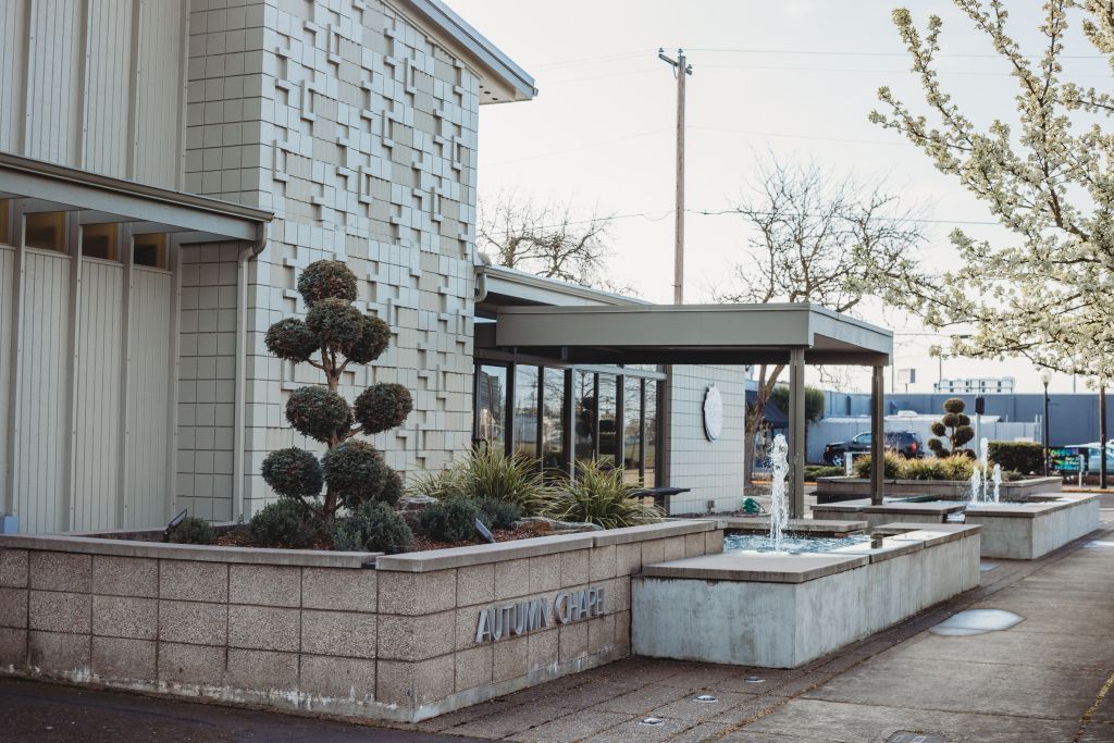 Exterior of a modern building with fountains and sculpted bushes. Light-colored concrete and decorative facade.