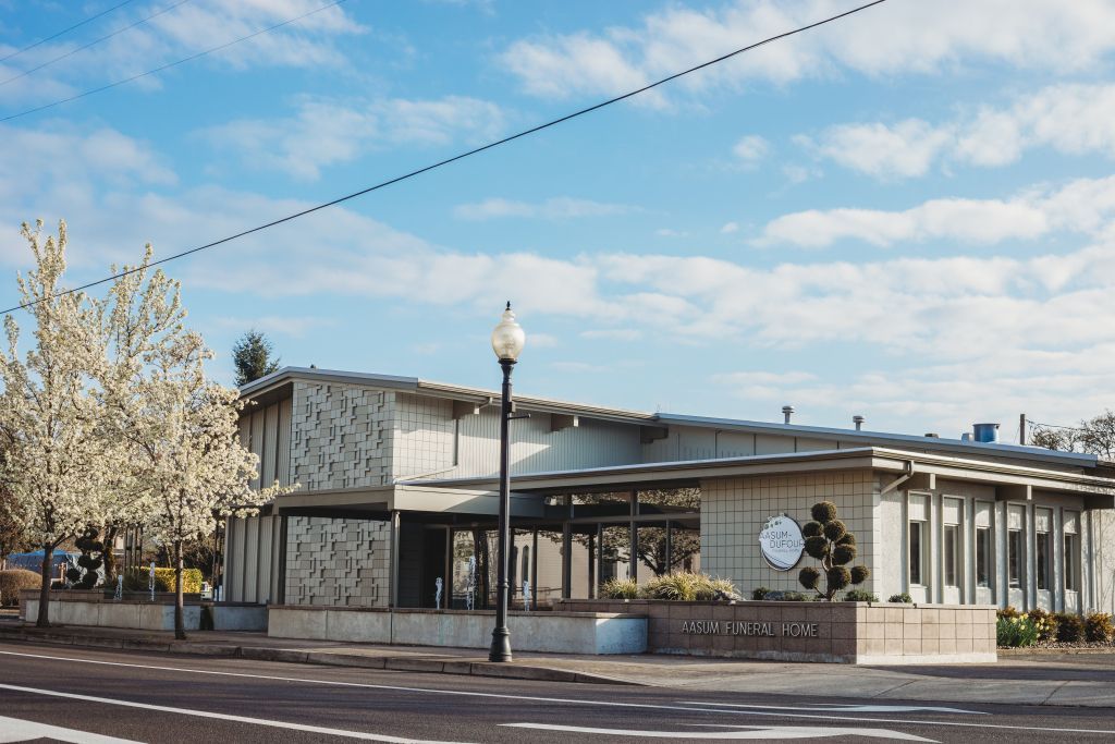 Modern building with light-colored facade, long windows, and a circular emblem, under a blue sky.
