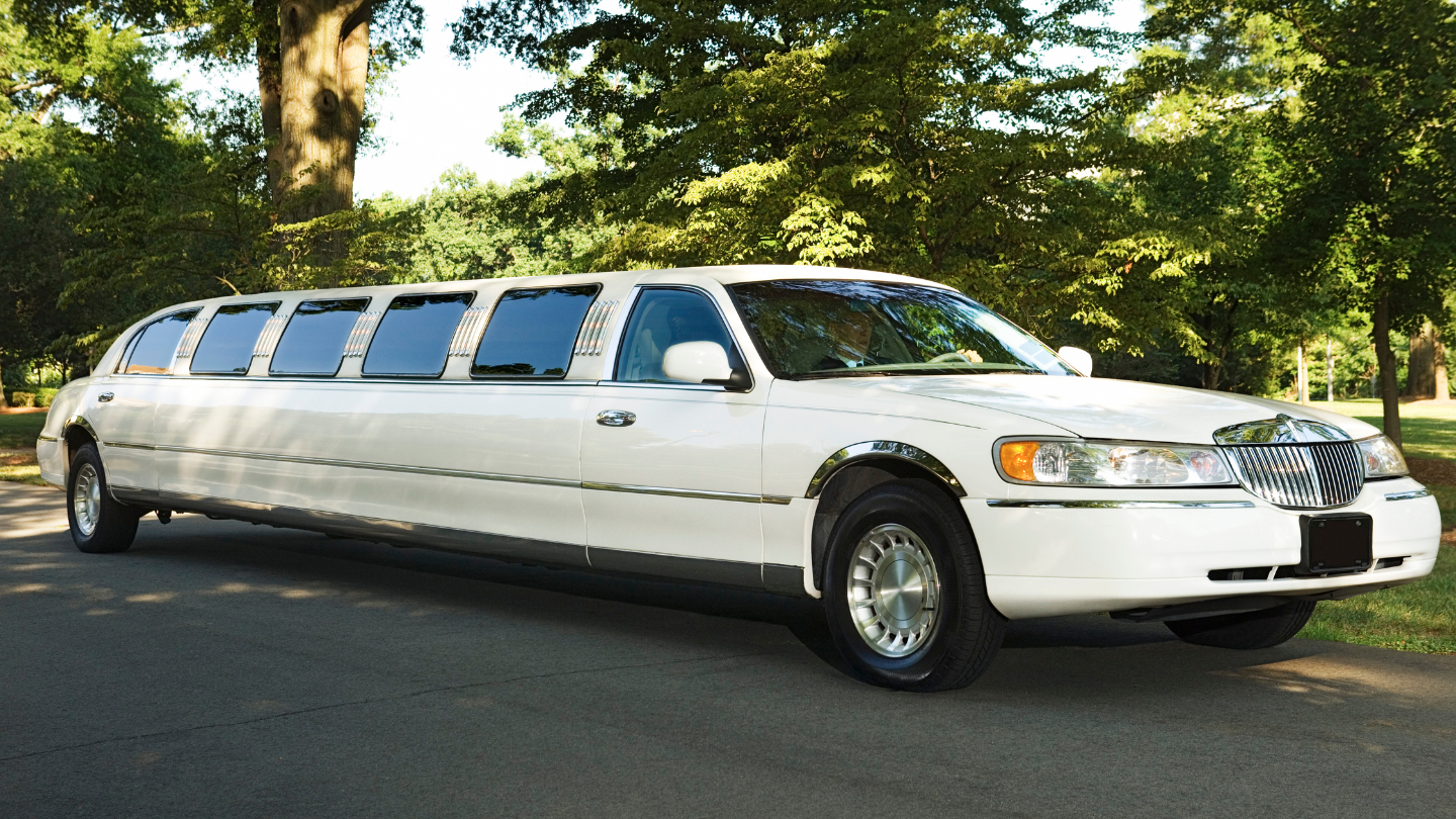 White limousine parked on a paved road, trees in the background.