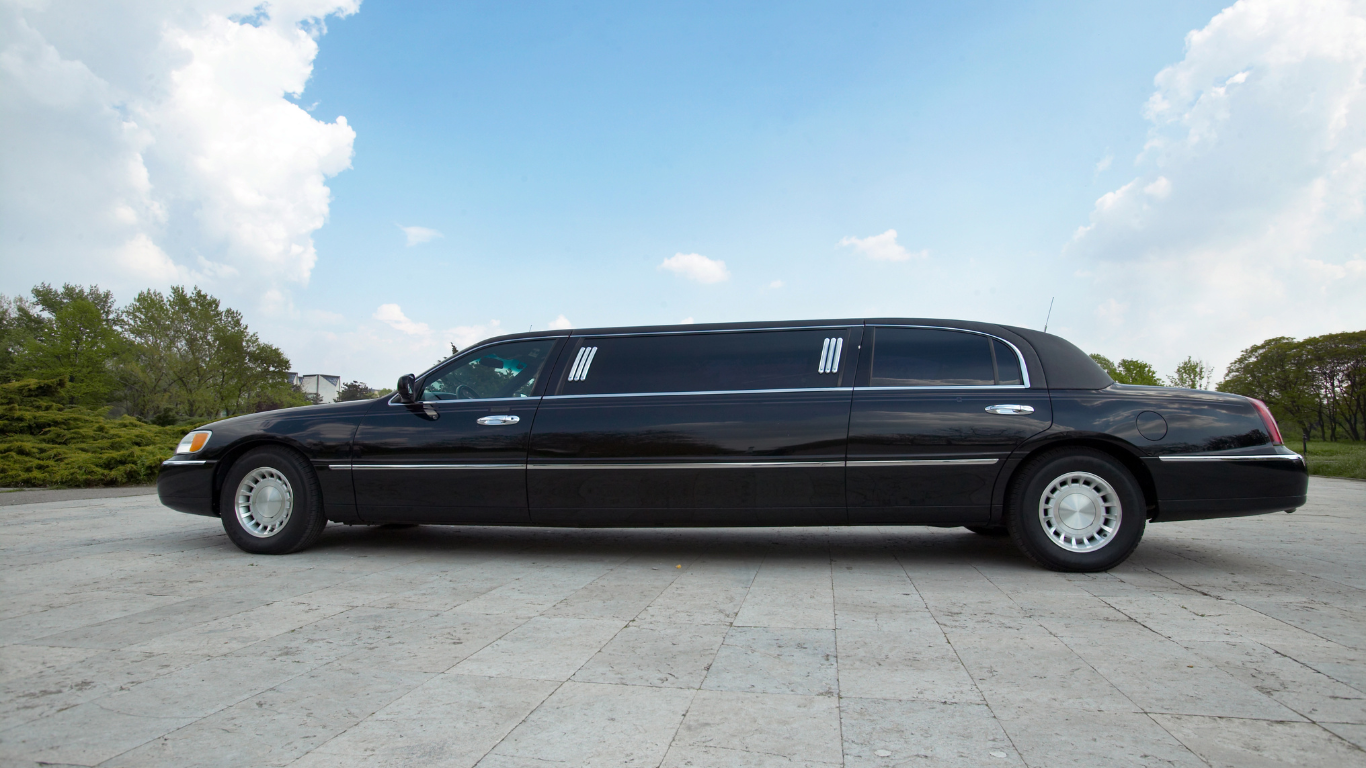 Black limousine parked on concrete, blue sky with clouds in the background.