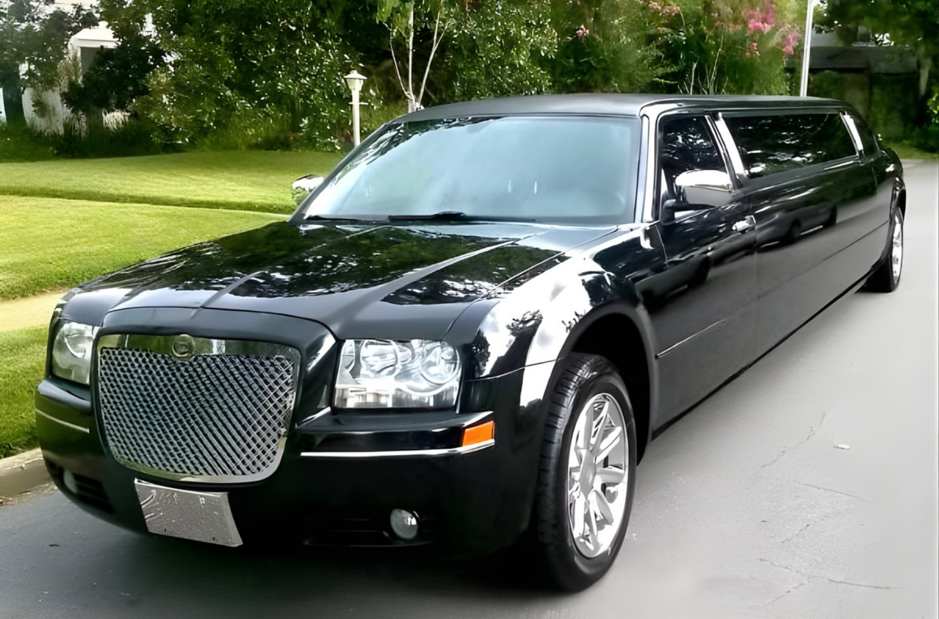 Black Chrysler 300 limousine parked on a paved driveway with green grass and trees in the background.