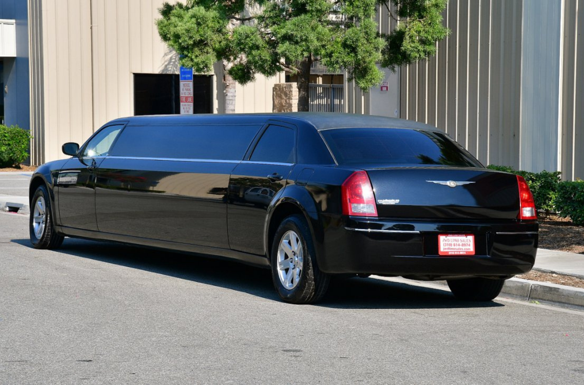 Black limousine parked on a paved road, next to a building.
