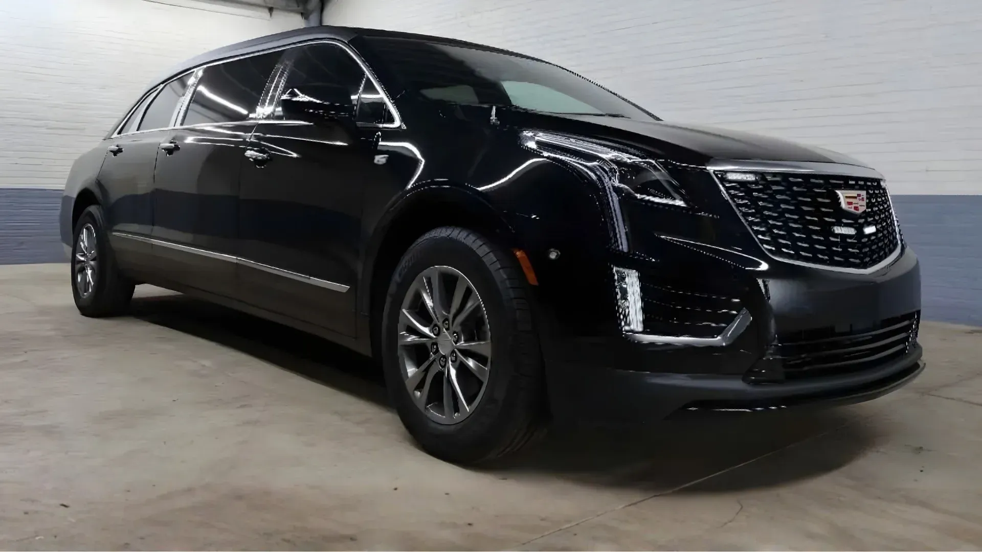 Black Chrysler limousine with white floral arrangement on the roof, driving on a road with mountains in the background.