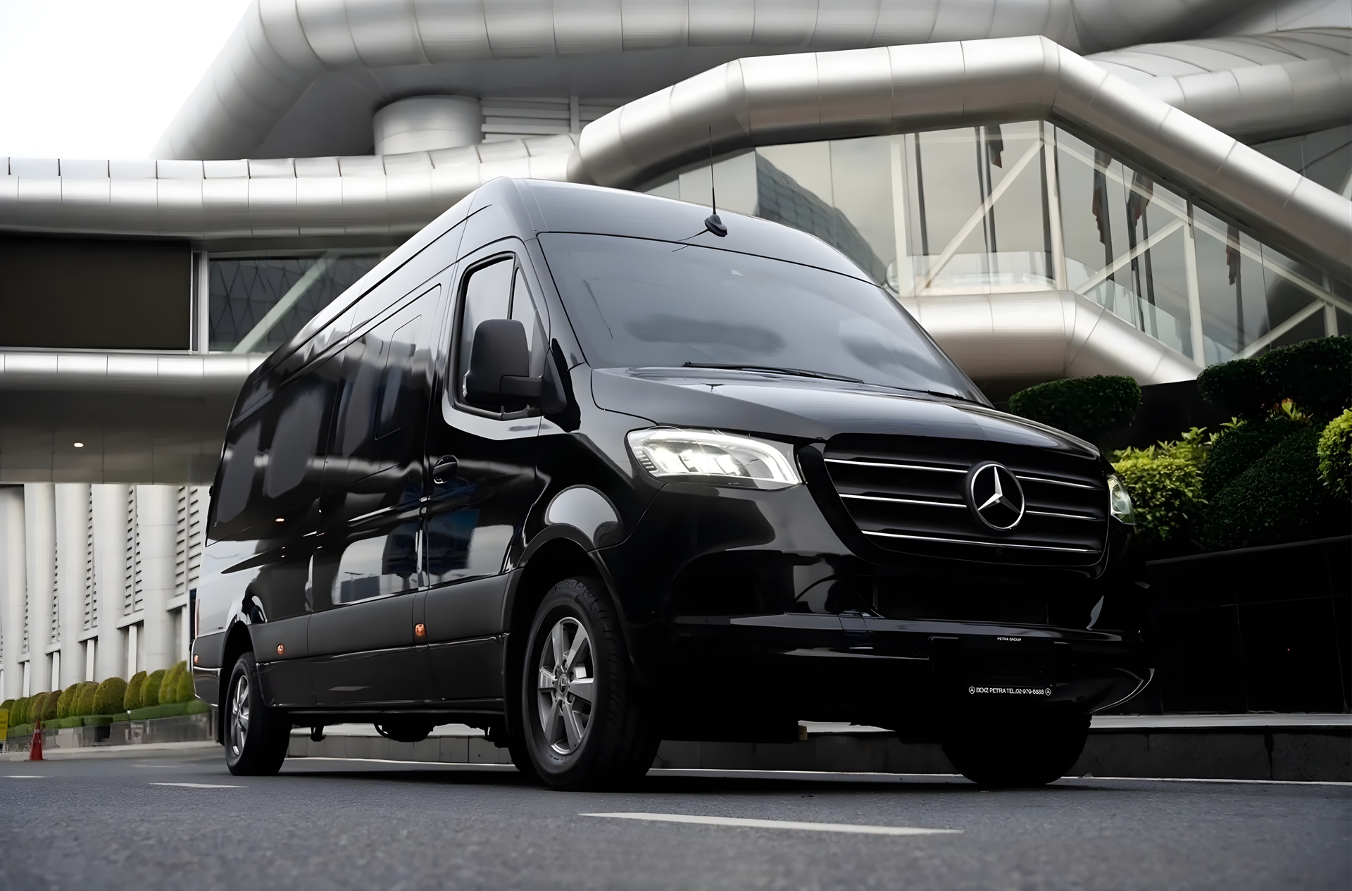 Black Mercedes van parked in front of a modern building with glass windows.