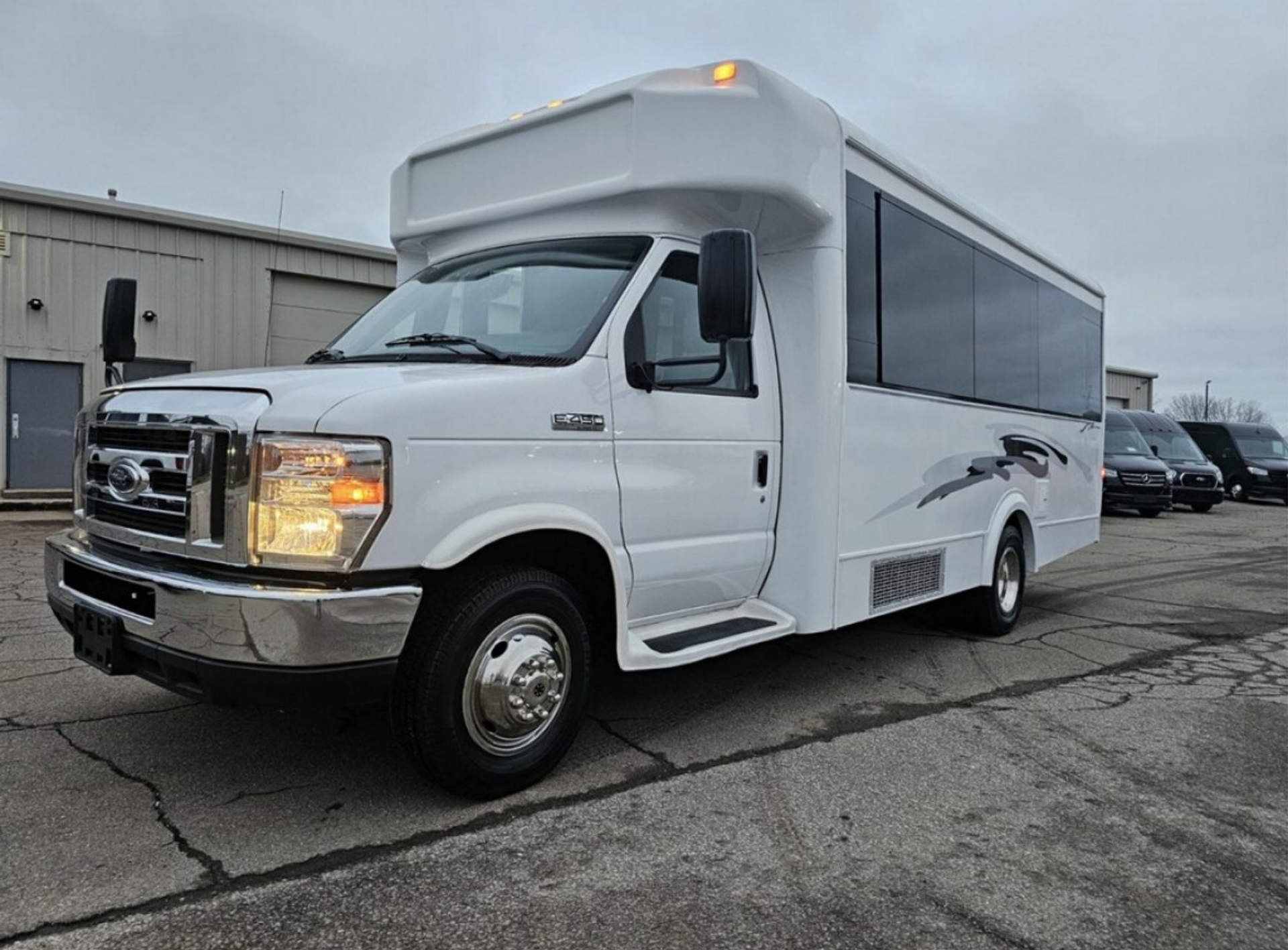 White passenger bus parked on a cracked concrete lot in front of a building.