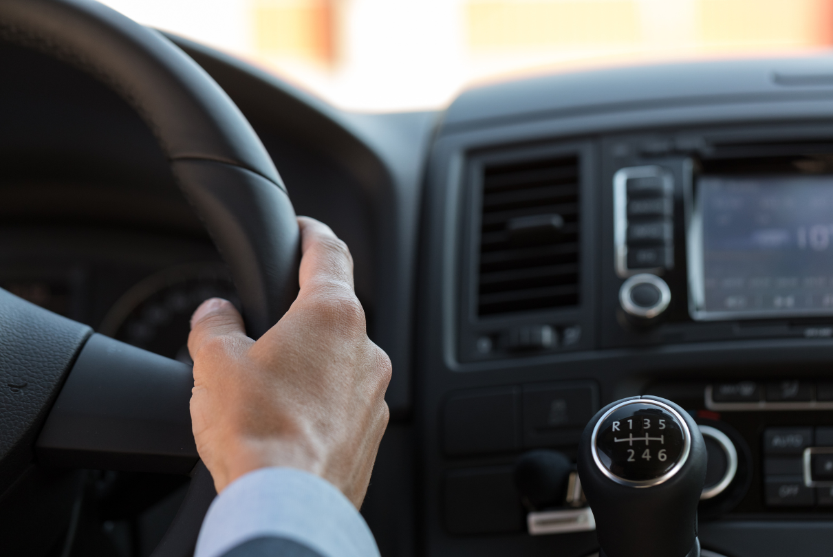 Hand gripping a black steering wheel inside a vehicle; gear shift visible.