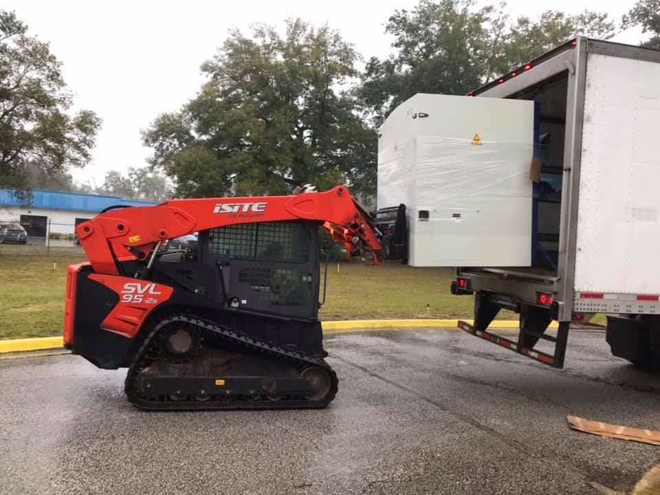 A small bulldozer is being towed by a truck. 28.4845° N, 81.2519° W