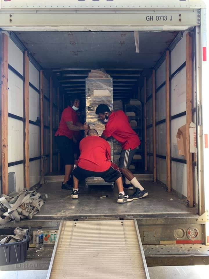 A group of men are pushing a large object into a moving truck. 28.4845° N, 81.2519° W