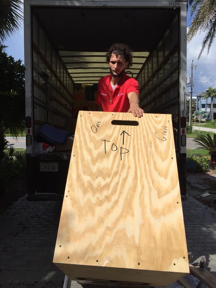 A man in a red shirt is holding a wooden box that says top on it