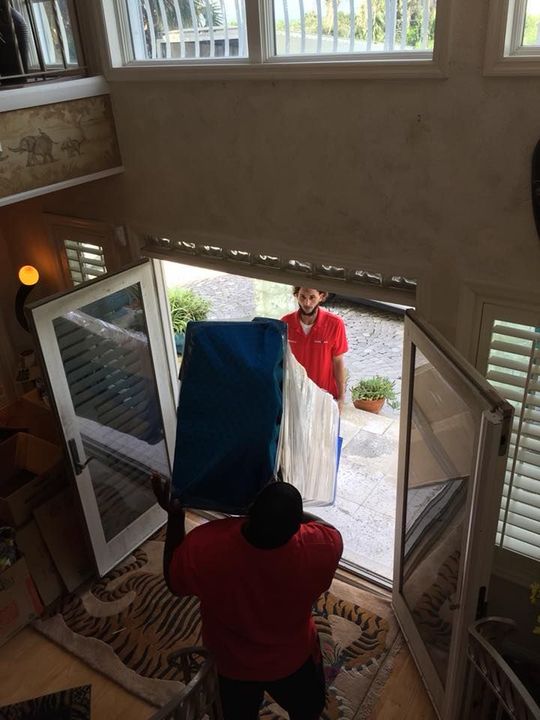 A man in a red shirt is carrying a blue box in a doorway. 28.4845° N, 81.2519° W