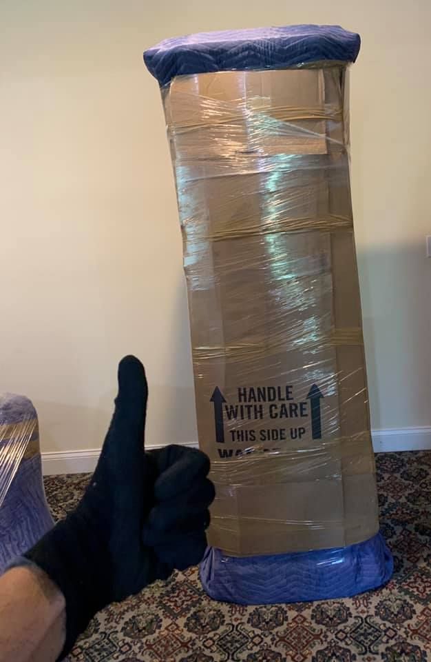 A person is giving a thumbs up in front of a cardboard box.