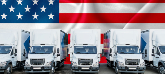 A row of white trucks are parked in front of an american flag.