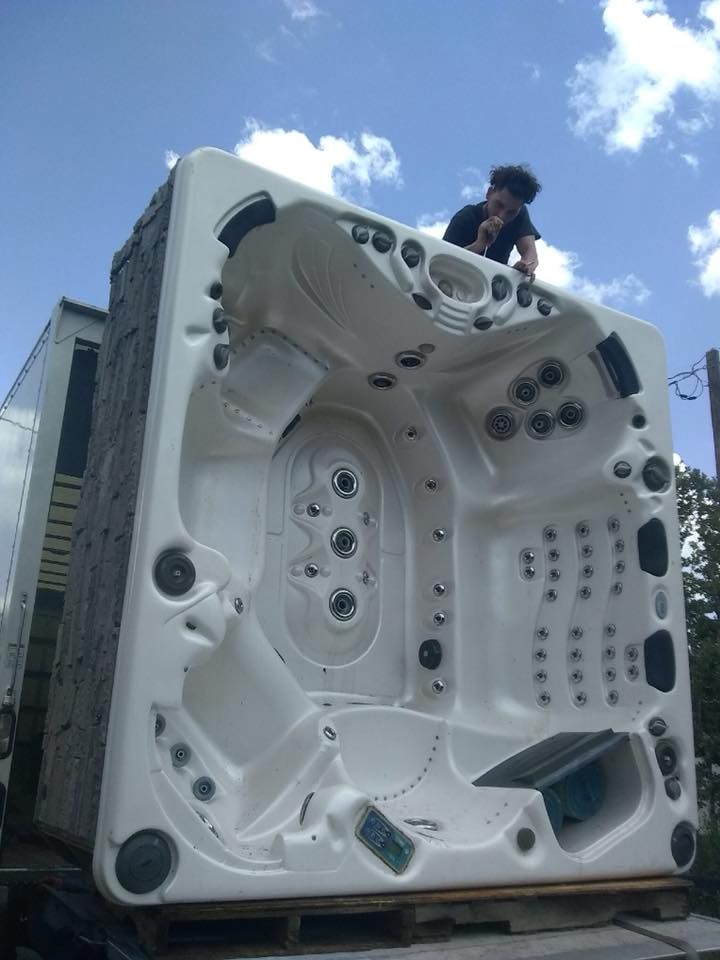 A man is standing on top of a large white hot tub