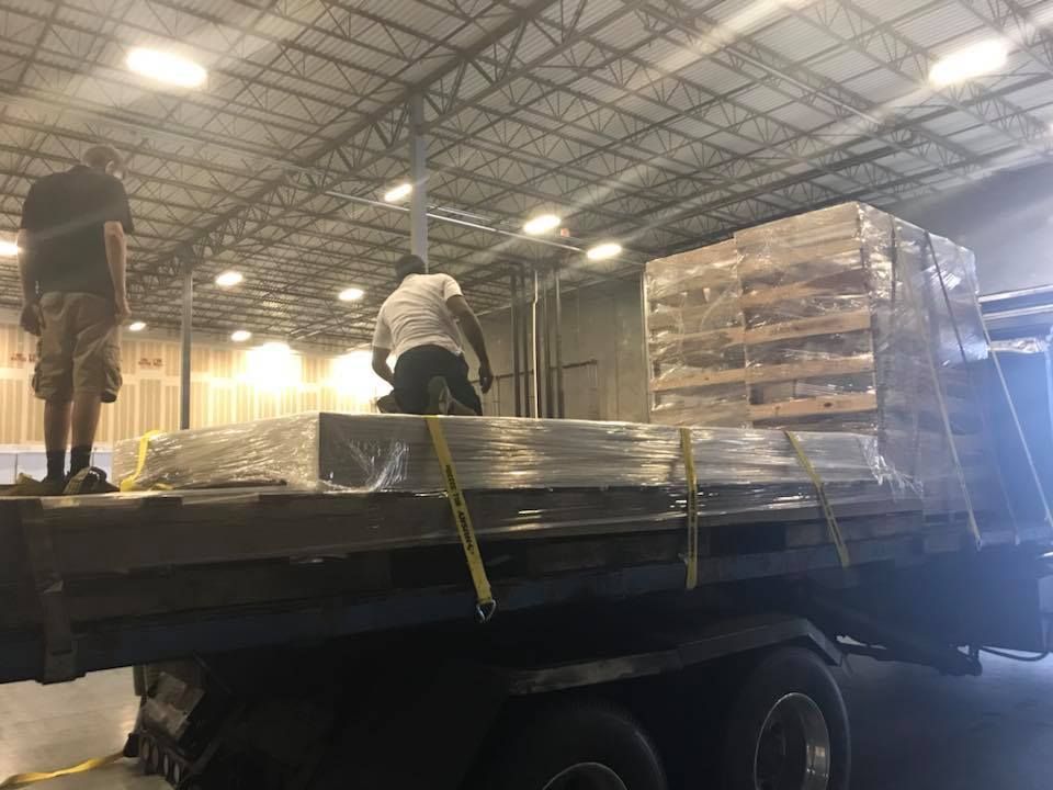 Two men are loading pallets onto a truck in a warehouse. 28.4845° N, 81.2519° W