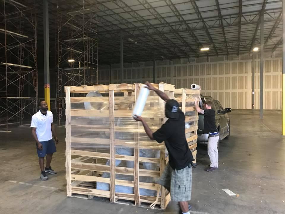 A man is wrapping a wooden crate with plastic wrap in a warehouse. 28.4845° N, 81.2519° W