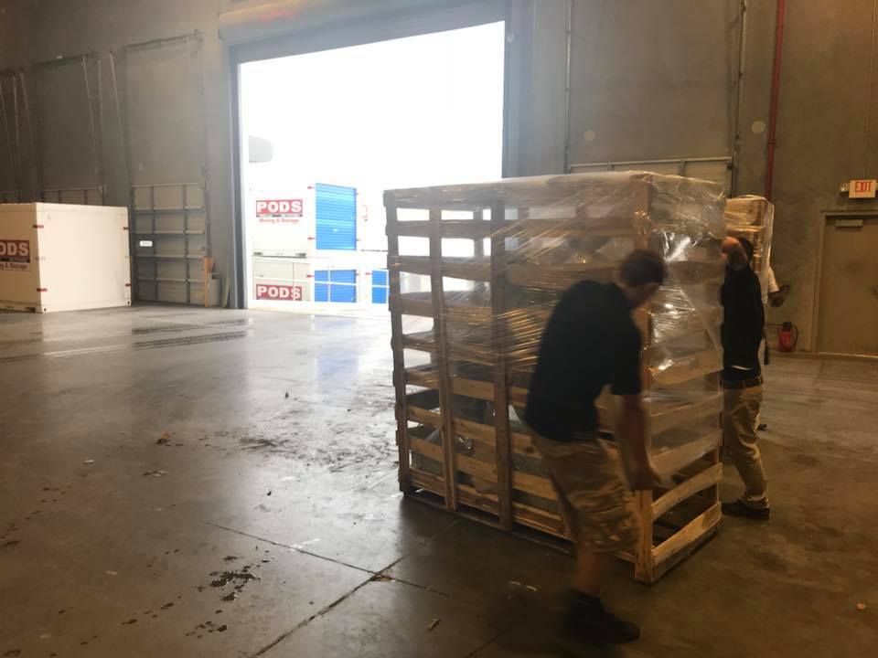 Two men are carrying a large wooden crate in a warehouse. 28.4845° N, 81.2519° W