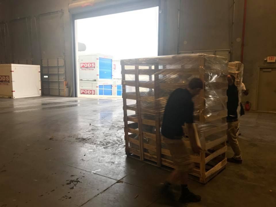 Two men are carrying a large wooden crate in a warehouse. 28.4845° N, 81.2519° W