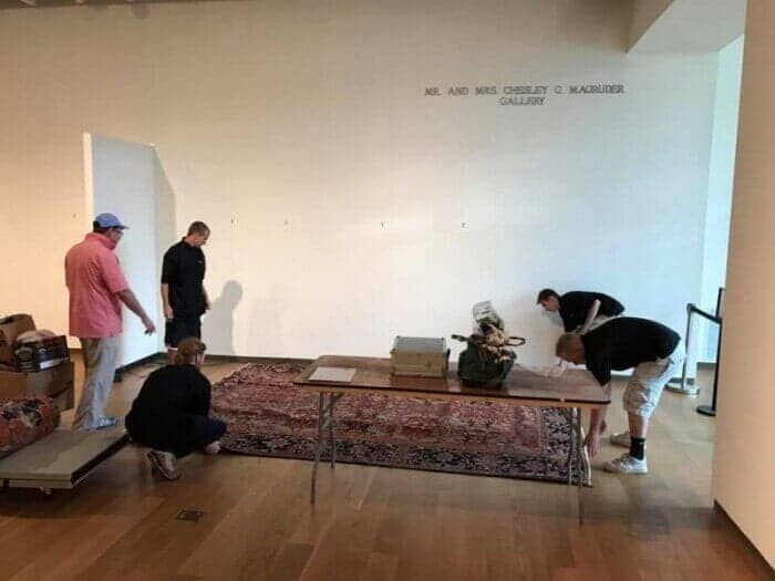 A group of people are working on a table in a room with a sign on the wall that says gallery 28.4845° N, 81.2519° W