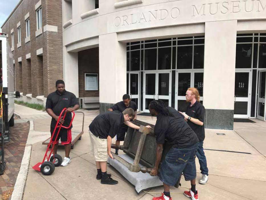 A group of men are moving a couch in front of the Orlando museum. 28.4845° N, 81.2519° W