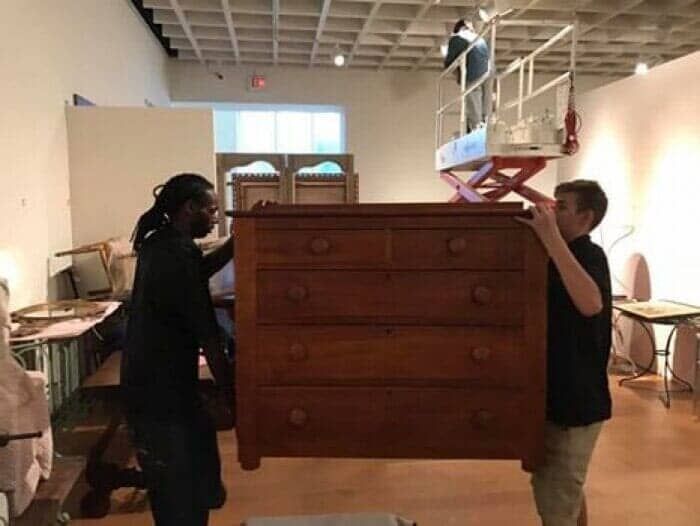 Two people are carrying a large wooden chest of drawers 28.4845° N, 81.2519° W