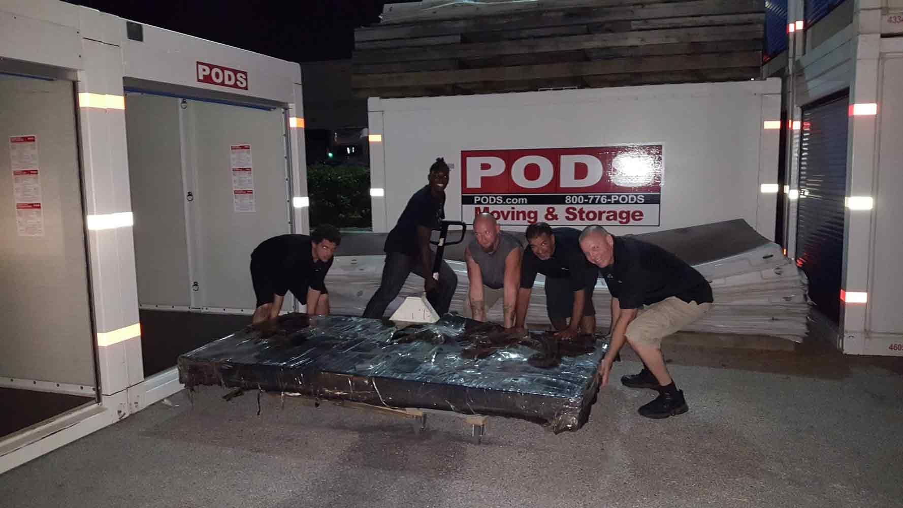 A group of men are working on a mattress in front of a pod moving and storage truck. 28.4845° N, 81.2519° W