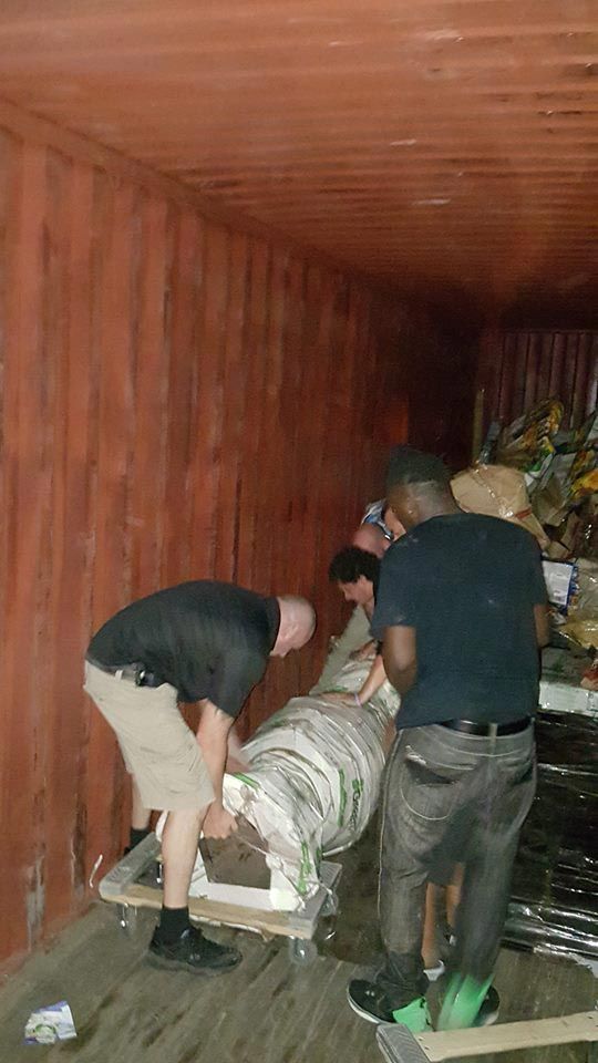 A group of men are moving a large object into a shipping container. 28.4845° N, 81.2519° W
