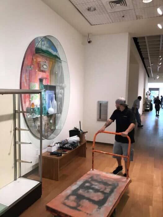 A man is pushing a cart in a museum with a painting on the wall behind him 28.4845° N, 81.2519° W