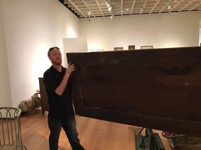 A man is holding a large piece of wood in a room 28.4845° N, 81.2519° W