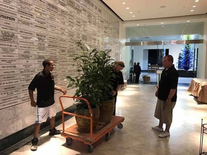 A group of men are pushing a cart with potted plants on it. 28.4845° N, 81.2519° W