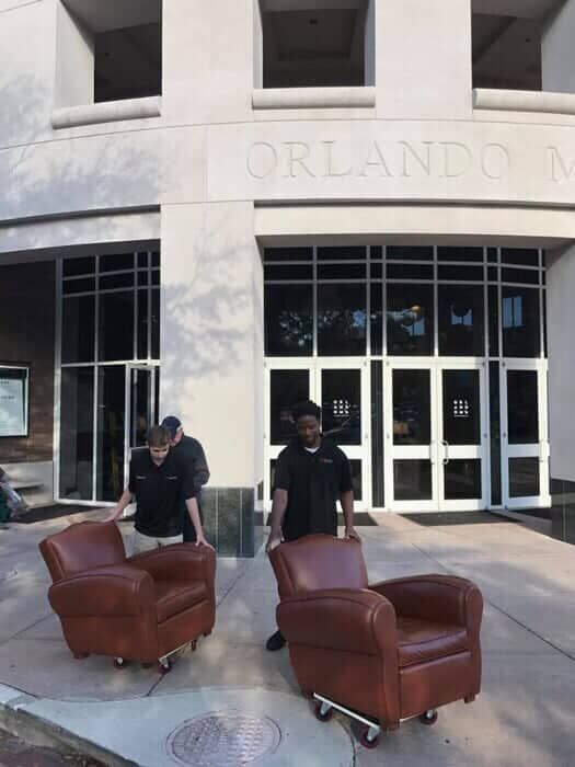 Two men are moving chairs in front of a building that says orlando 28.4845° N, 81.2519° W