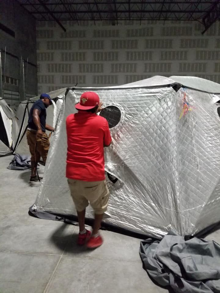 A man in a red shirt is standing next to a tent in a warehouse. 28.4845° N, 81.2519° W