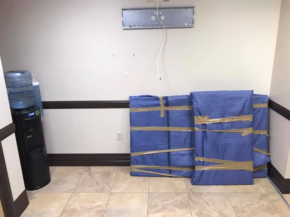 A room with a water cooler and a couch wrapped in blue plastic. 28.4845° N, 81.2519° W