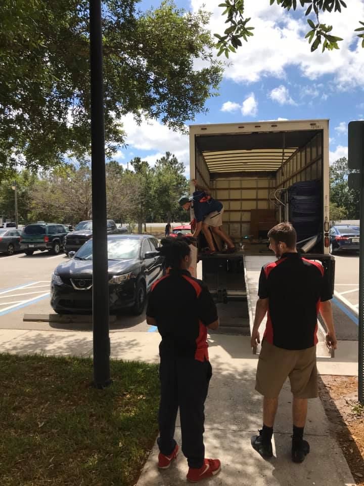 Two men are standing next to a moving truck in a parking lot. 28.4845° N, 81.2519° W