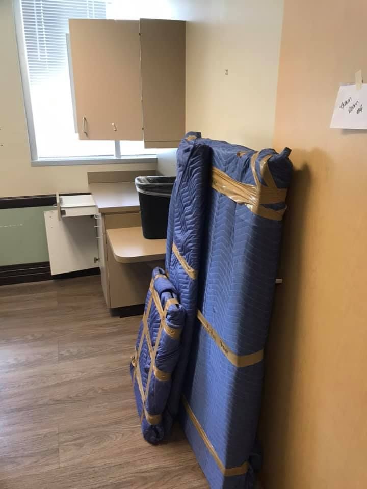 A blue mattress is wrapped in plastic and taped to a wall in a room. 28.4845° N, 81.2519° W