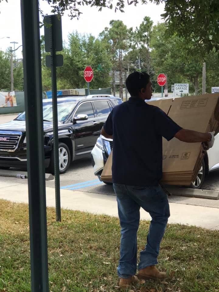 A man is carrying a large cardboard box in front of a stop sign 28.4845° N, 81.2519° W