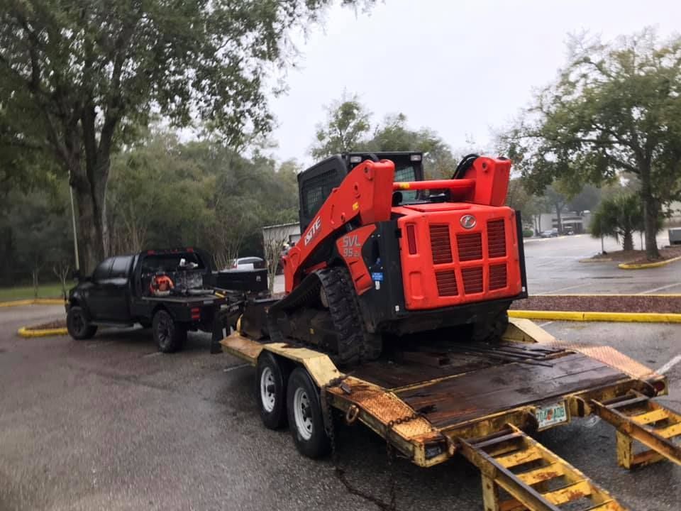 A truck is towing a skid steer on a trailer. 28.4845° N, 81.2519° W