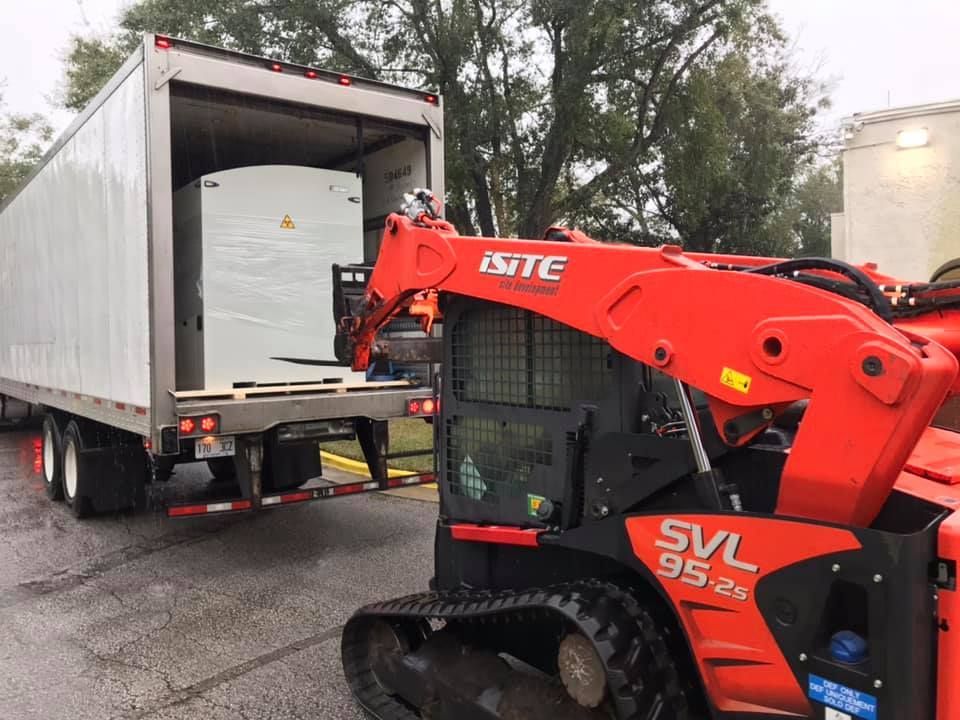 A skid steer is being towed by a semi truck.28.4845° N, 81.2519° W