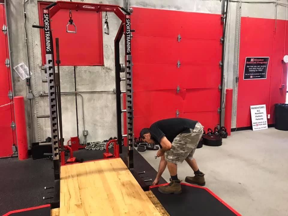 A man is squatting on a wooden floor in a gym. 28.4845° N, 81.2519° W