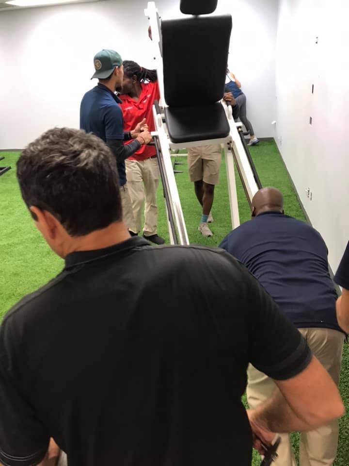 A group of men are standing around a chair in a gym 28.4845° N, 81.2519° W