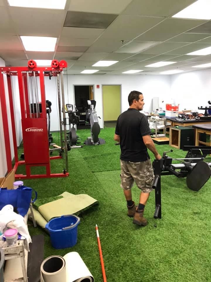 A man is standing in a gym with a red machine. 28.4845° N, 81.2519° W