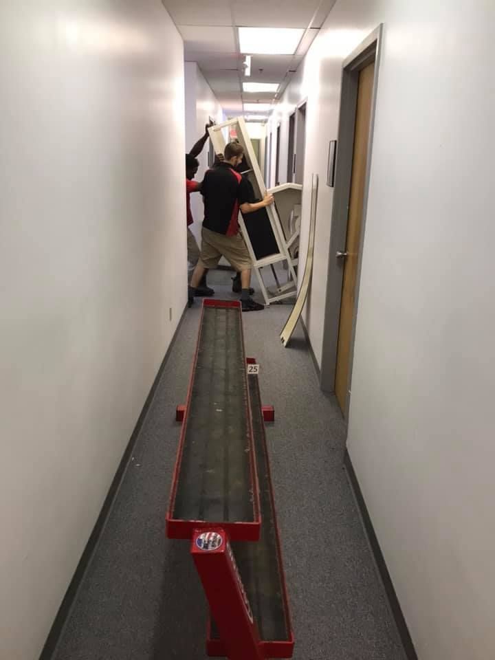 A man is carrying a large piece of furniture down a hallway. 28.4845° N, 81.2519° W