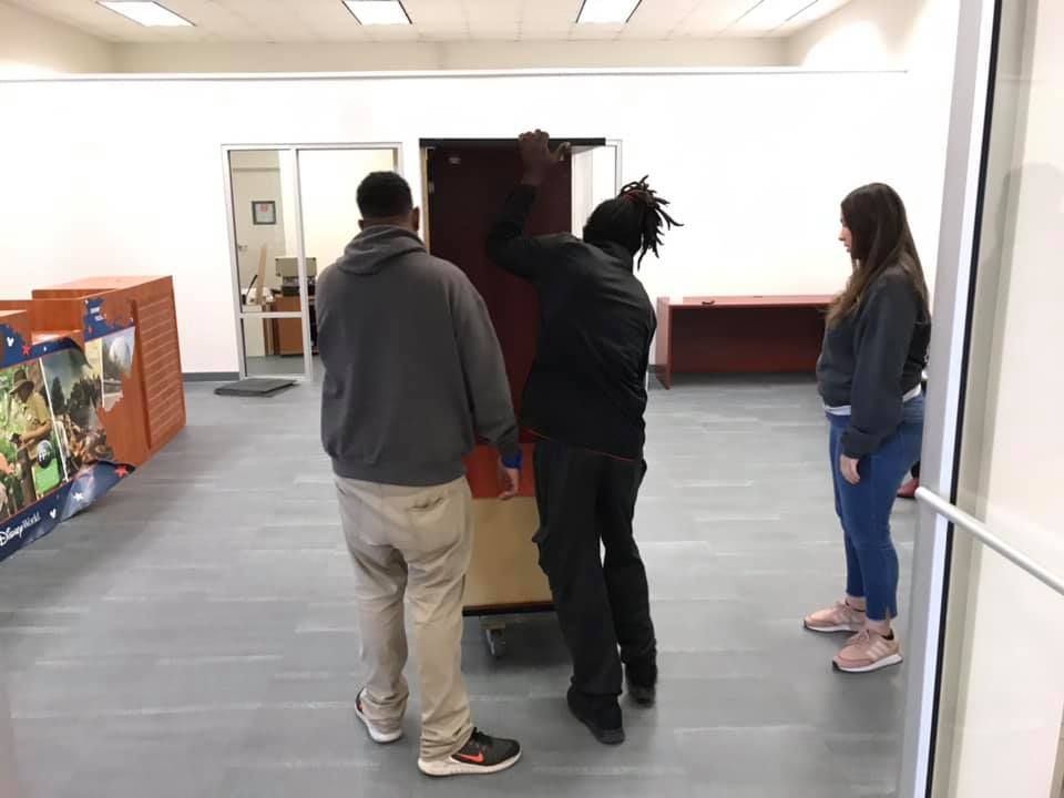 A group of people are moving a cabinet in a room. 28.4845° N, 81.2519° W