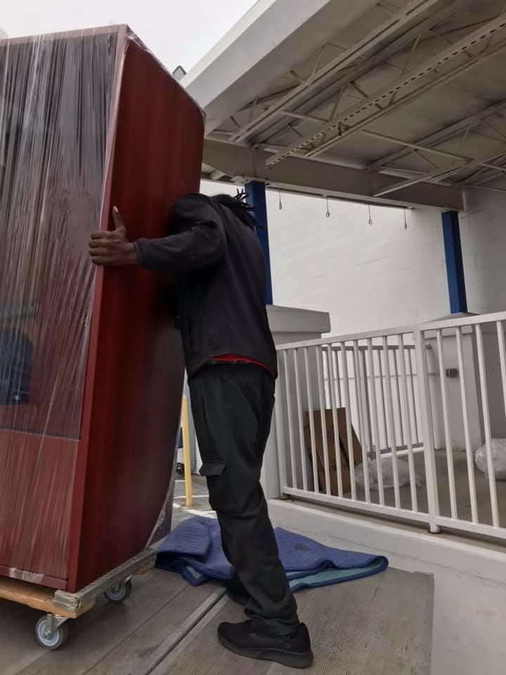 A man is carrying a large piece of furniture on a cart. 28.4845° N, 81.2519° W