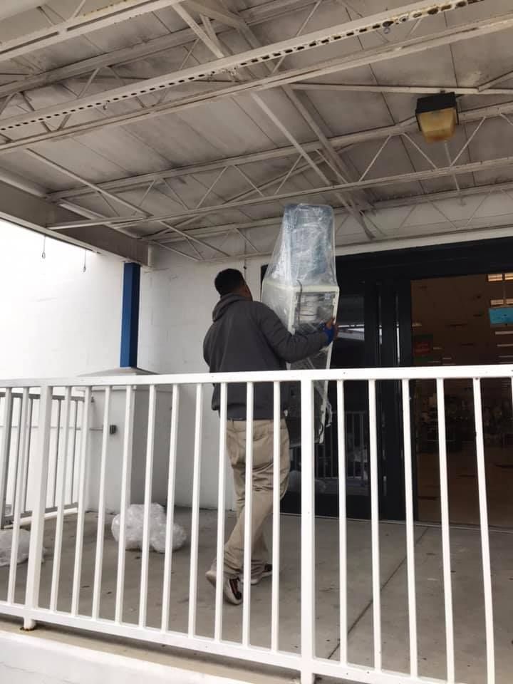 A man is carrying a refrigerator outside of a building. 28.4845° N, 81.2519° W