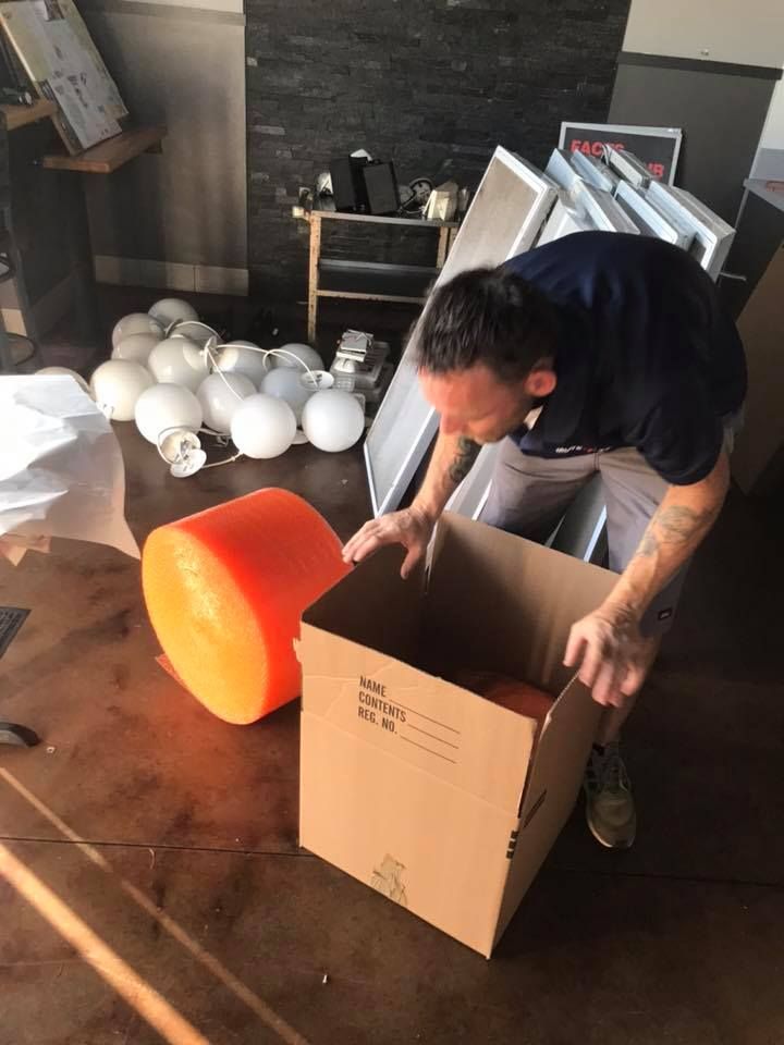 A man is opening a cardboard box in a messy room. 28.4845° N, 81.2519° W